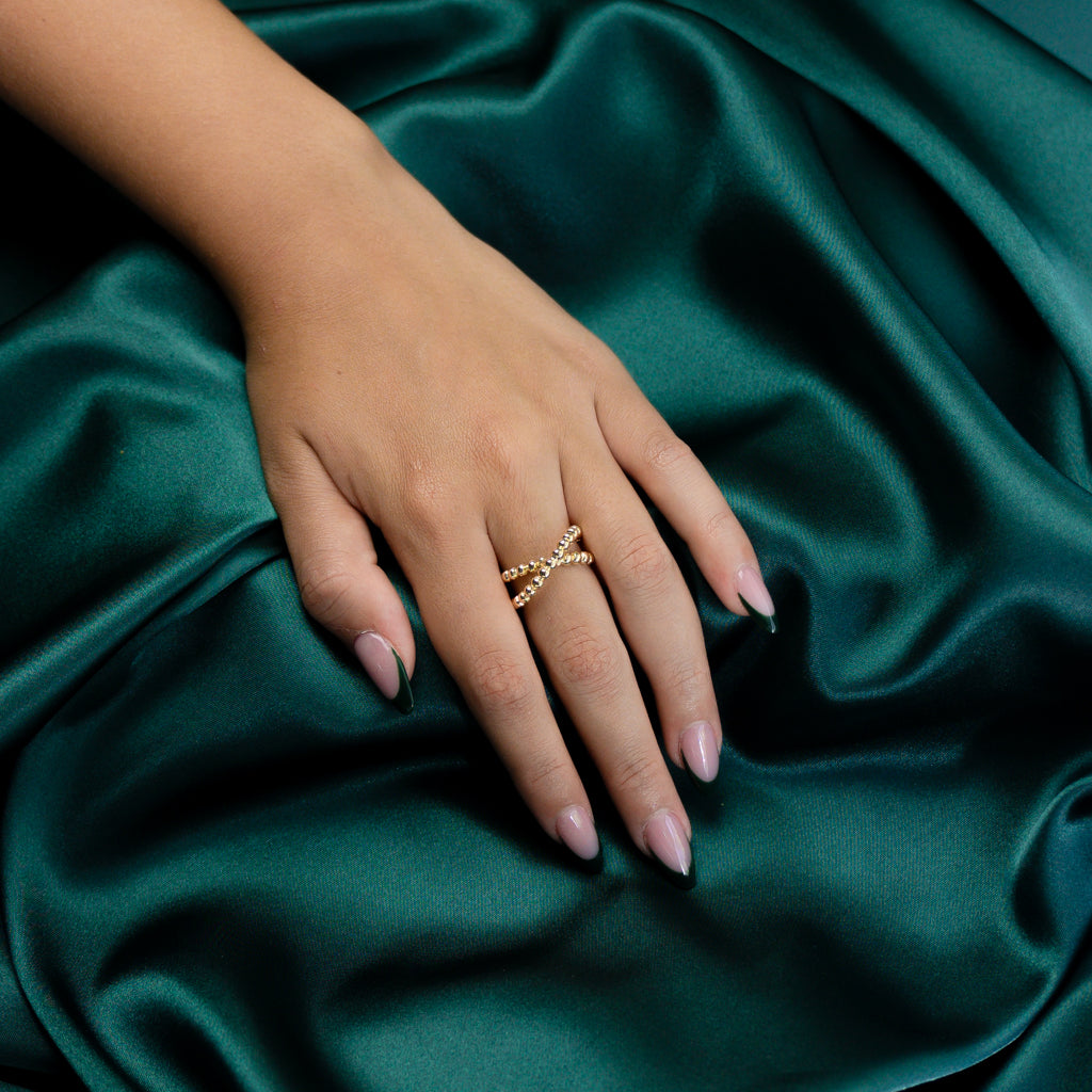 Angled perspective of a model wearing the Beaded Criss Cross Ring against a green backdrop.