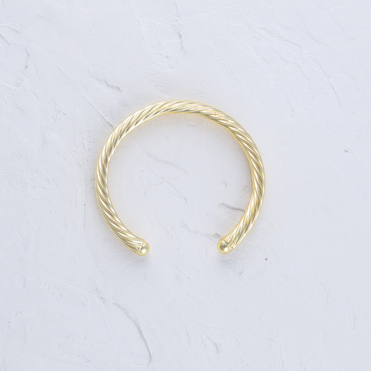 Twisted Gold Bangle lying flat on a white background